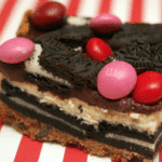 OREO CHEESECAKE BARS ON A CHOCOLATE CHIP COOKIE CRUST TOPPED WITH A CHOCOLATE GLAZE, RASPBERRY M & M’S AND MORE OREOS!